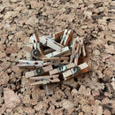 Små træclips med metalnål på korkoverflade, ligner miniature-tøjklemmer, flere i en bunke.