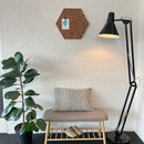 Sekskantet korktavle på væg, med rustik tekstur. Ved siden af er en plante, bænk og gulvlampe.
