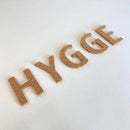 Bogstaverne "HYGGE" i kork på en lys overflade.
