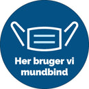 Rundt gulvklistermærke med hvidt ikon af mundbind og teksten "Her bruger vi mundbind" på dansk.